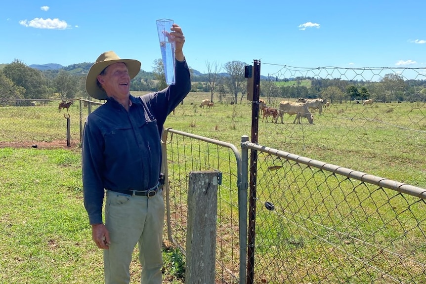 A farmer smiles holding up a rain gauge full of water.