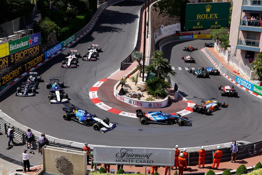 F1 cars going around a hairpin corner on a street track.
