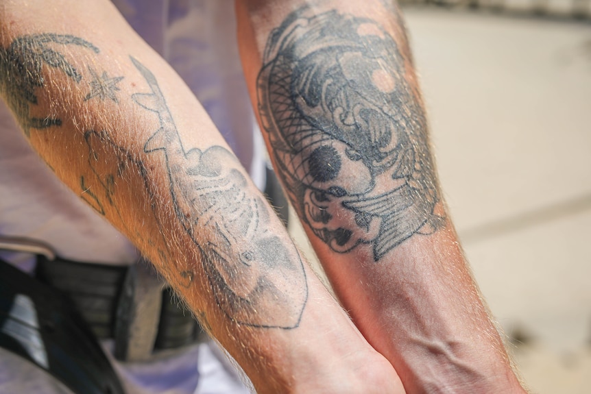 A man's arms showing several ocean-inspired tattoos including a ray and some fish.