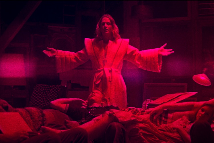 Colour still of Richard Brake, Ned Dennehy, Linus Roache and two others in a red tinted living room in 2018 film Mandy.