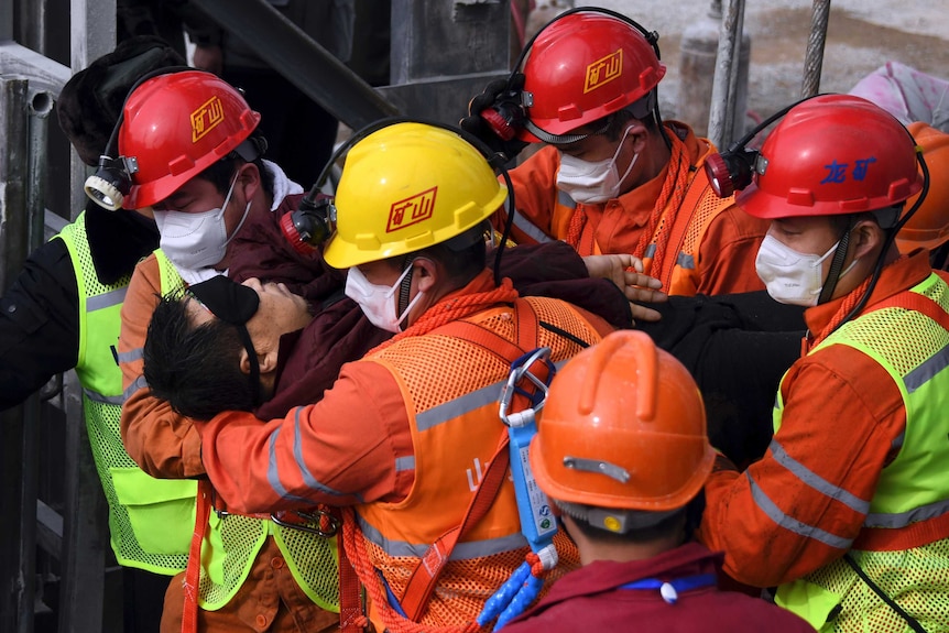 Rescue workers wearing high-vis and hardhats carry a person in their arms.