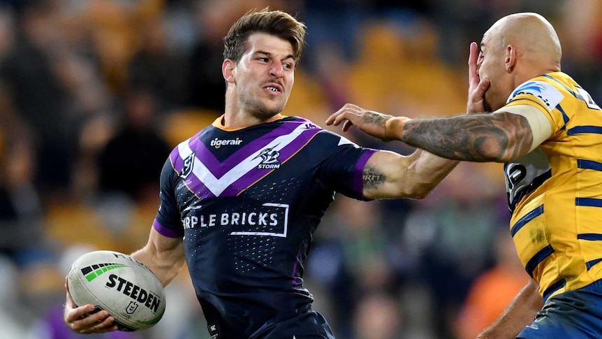 A man with a football pushes his palm into another man's face as he tried to evade a tackle.