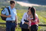 A picture from Home and Away being filmed. The characters Alex and Willow kiss while a man in a police uniform watches.