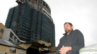 A man stands in front aof a large high-rise development.