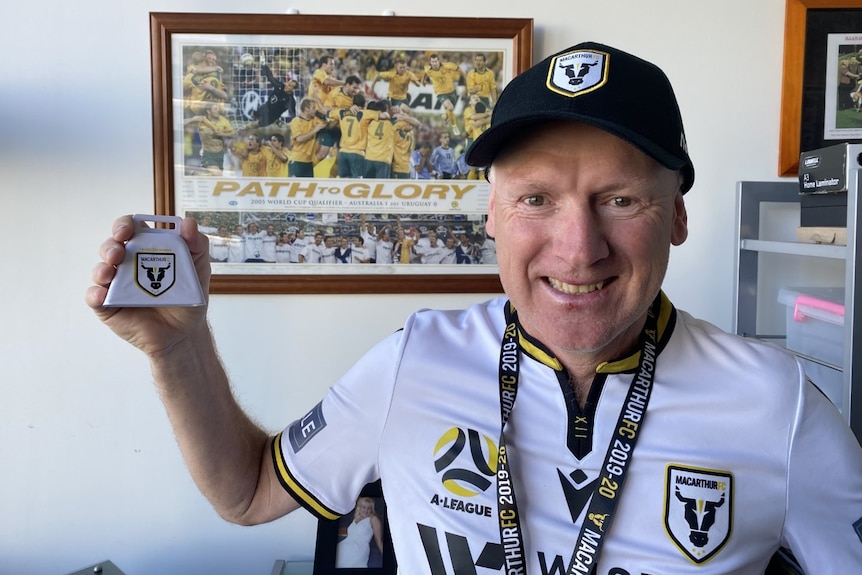 An older man wearing his football team's jersey and hat, smiling.