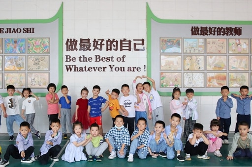 A group of 15 Chinese twins stand in summer clothing in front of a school classroom with Chinese writing