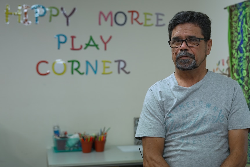 Lloyd Munro wearing glasses and a grey shirt in front of a play corner sign