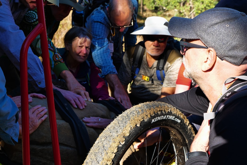 A group of people crouch around the wheel of a cart.