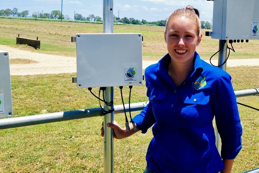 Women in blue workshirt stands next to an automated irrigation system. 