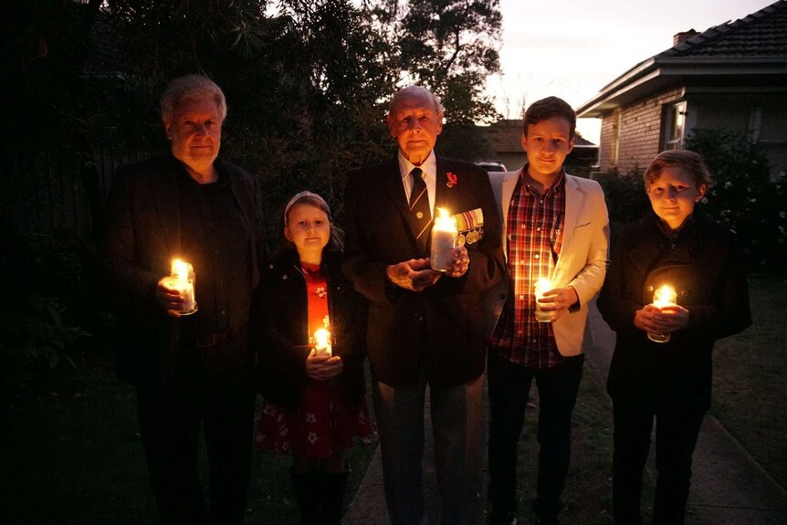 Three generations of the Sims family hold candles in a driveway to commemorate Anzac Day.