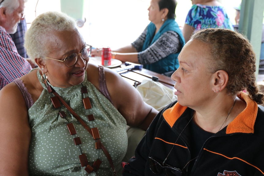 Two south sea islander women sit at park table in conversation. 