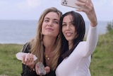 Two young women holding crystals take a selfie in front of the ocean