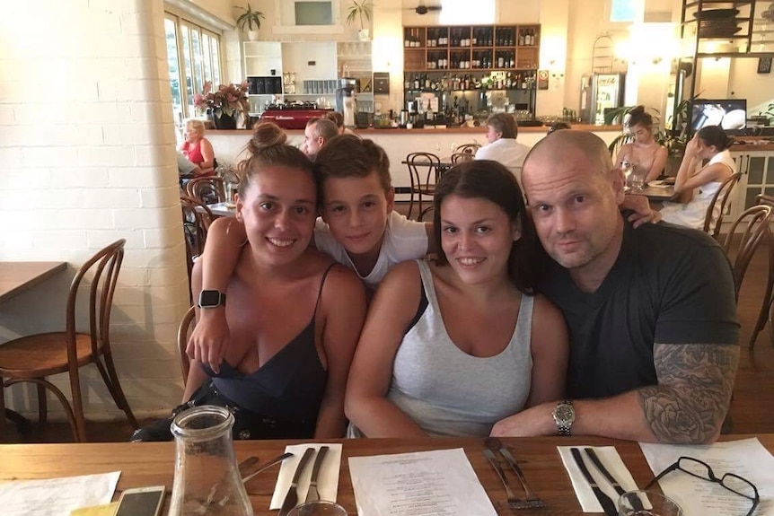 Dave Roberts and his children all sitting on one side of a table in a large cafe, with the bar and counter in the background