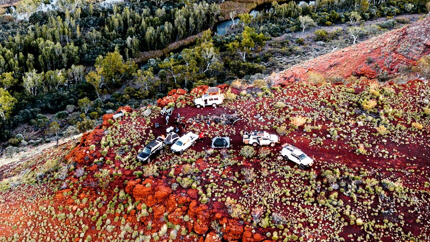 A drone photo of a campsite on the red dirt of the Pilbara, beside a creek.