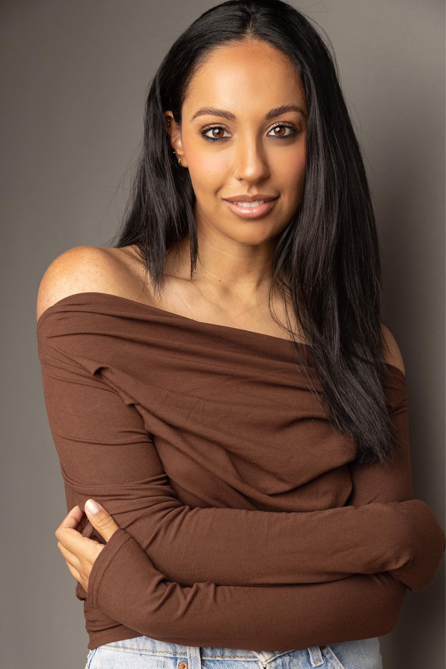 A woman with black hair wearing a brown top smiles at the camera 