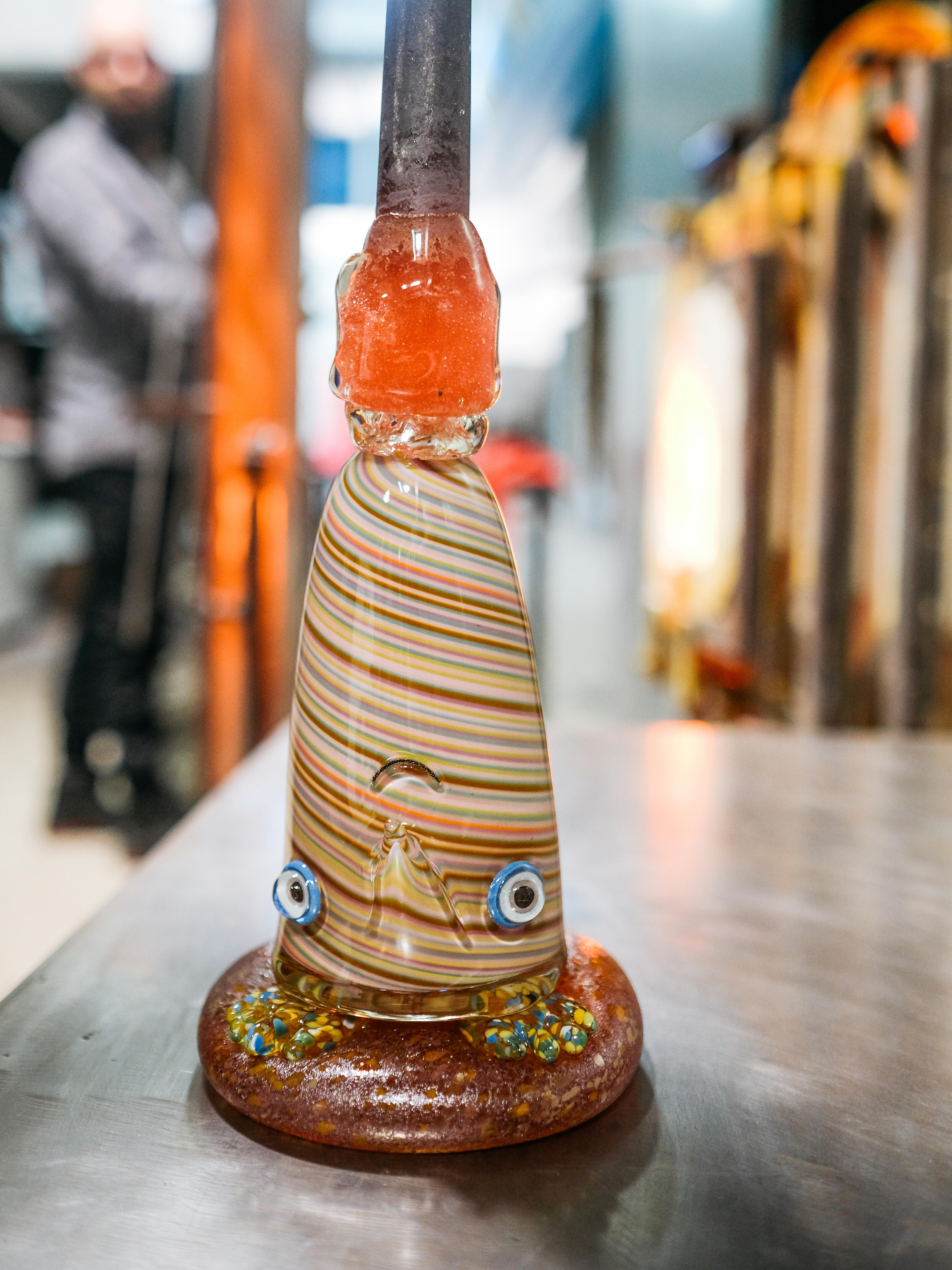 A glass sculpture upside down on the workshop bench - it looks like a character, with googly eyes and a little mouth