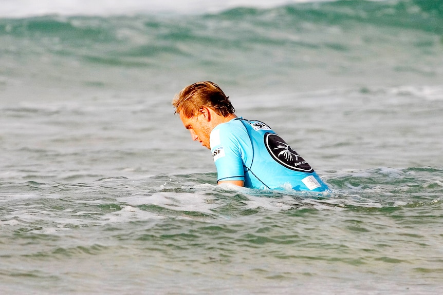 a man on  a surfboard out in the water looking dejected