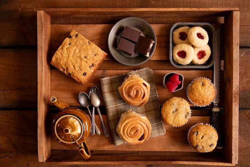 a wooden box filled with baked goods, a tea pot, tea spoons 