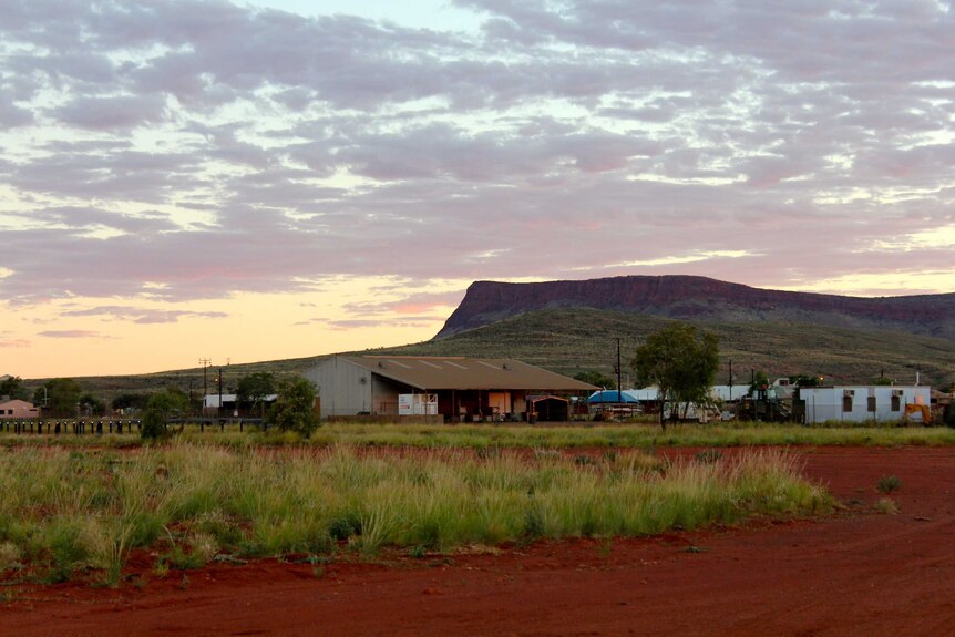 A few buildings at Kintore in the foreground of a mountain range at sunset.