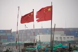 Two Chinese flags flutter in the wind at a shipping port.