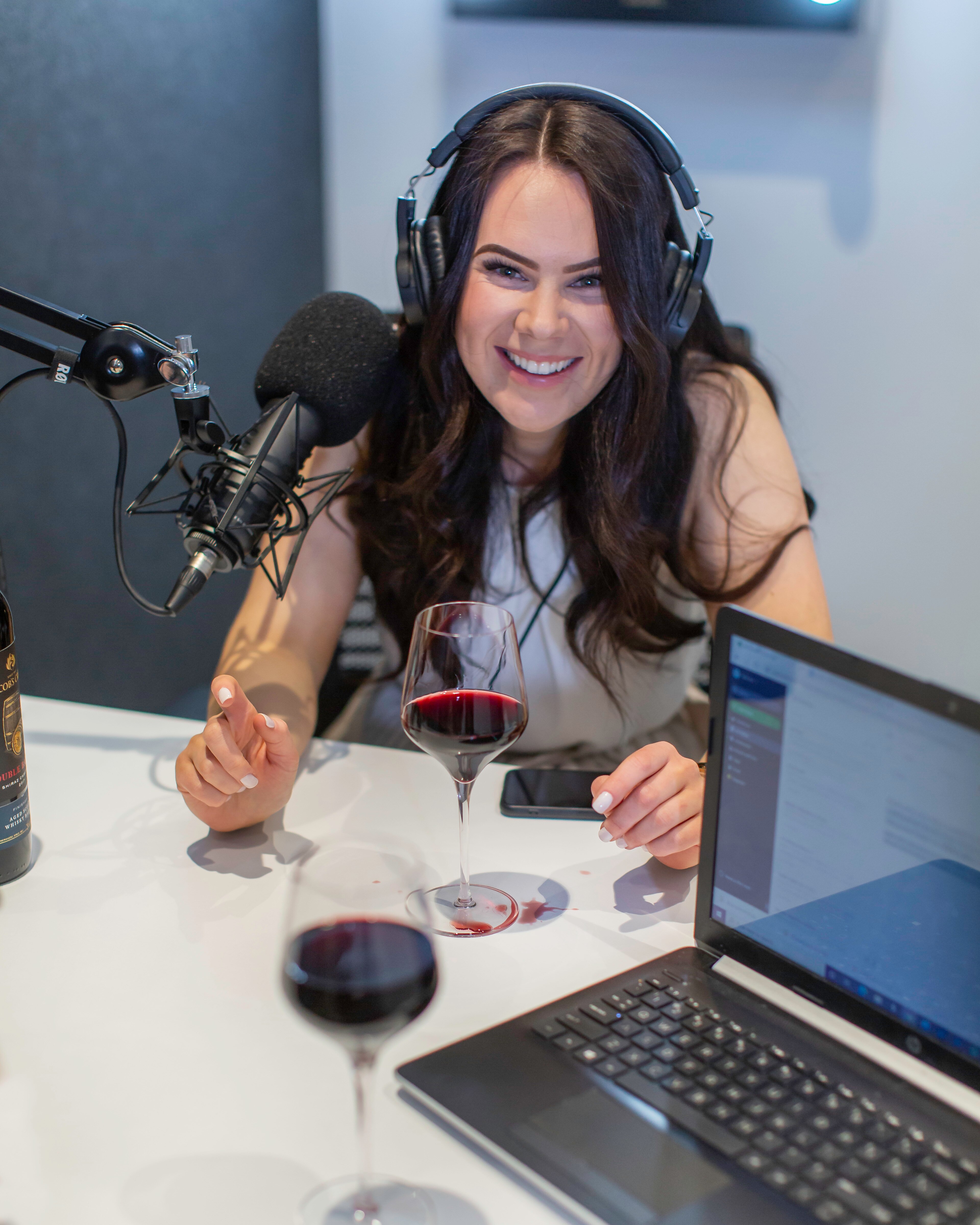 Victoria Devine sits in a sound recording space with a large microphone and a glass of red wine in front of her. 