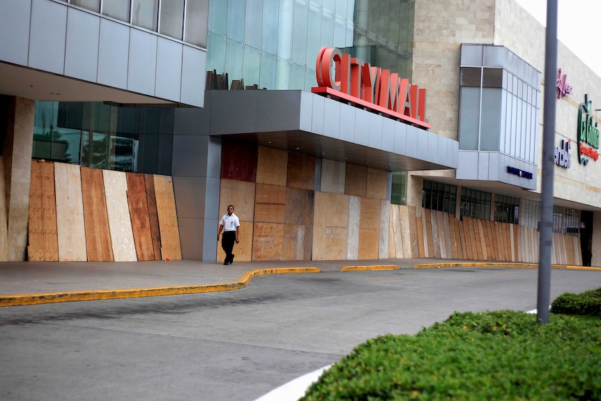 A man walks past a shopping centre with boards covering its front windows.