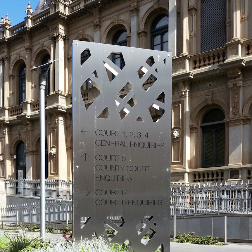 A metal sign in garden bed displaying details of the court in the building behind