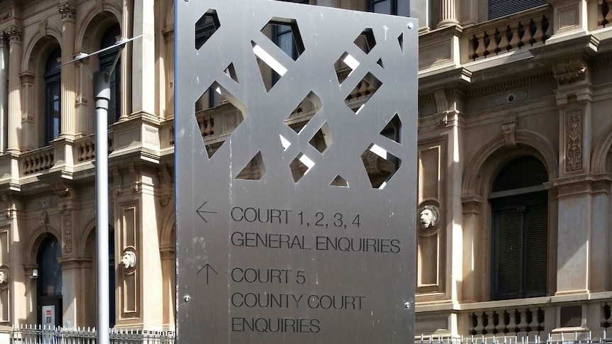 A metal sign in garden bed displaying details of the court in the building behind