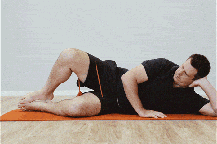 A man lying on a mat and demonstrating how to a clamshell exercise to strengthen his muscles for standing up for long periods.