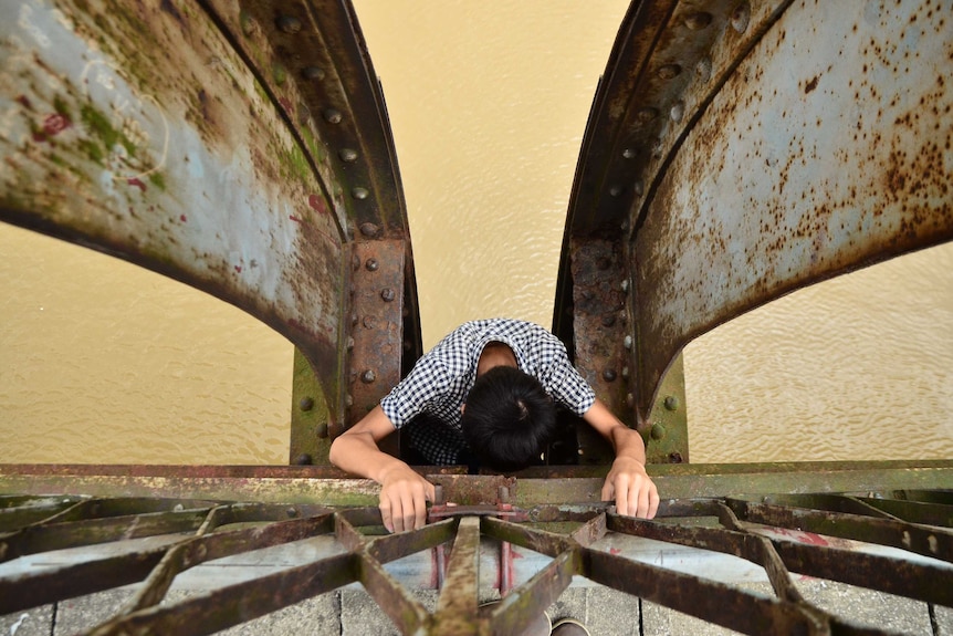 Looking down at a boy climbing down a ladder on a railway bridge