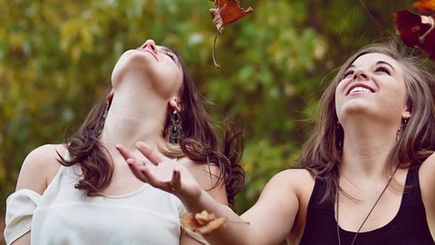 Two women frolic in autumn leaves.