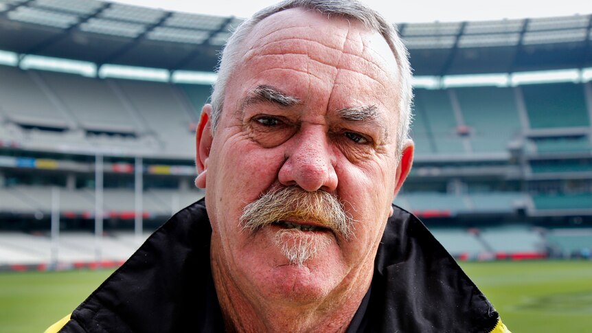 Former footballer Robert McGhie stares down the camera, wearing a jacket at the MCG.