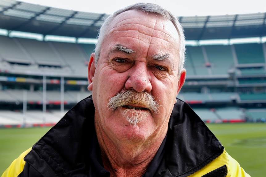 Former footballer Robert McGhie stares down the camera, wearing a jacket at the MCG.