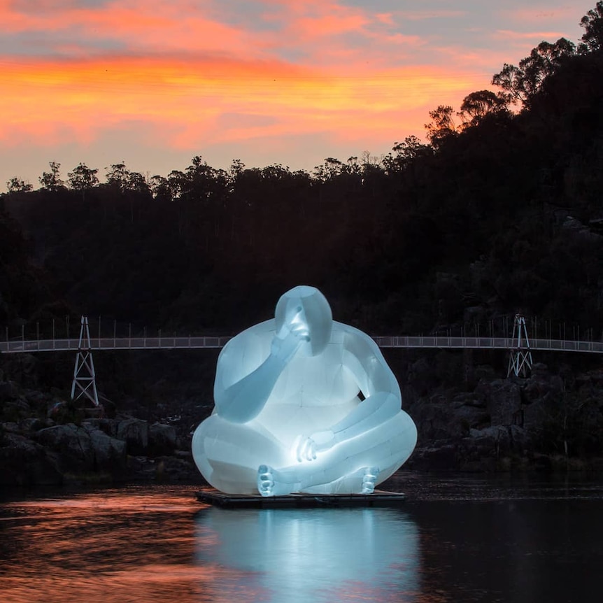 A huge inflatable sculpture of a thinking man sits in a pontoon in water.