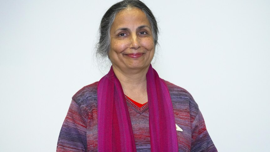 Woman wearing a purple scarf and purple jumper smiles at the camera