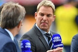 Shane Warne holding a microphone during Nine cricket coverage