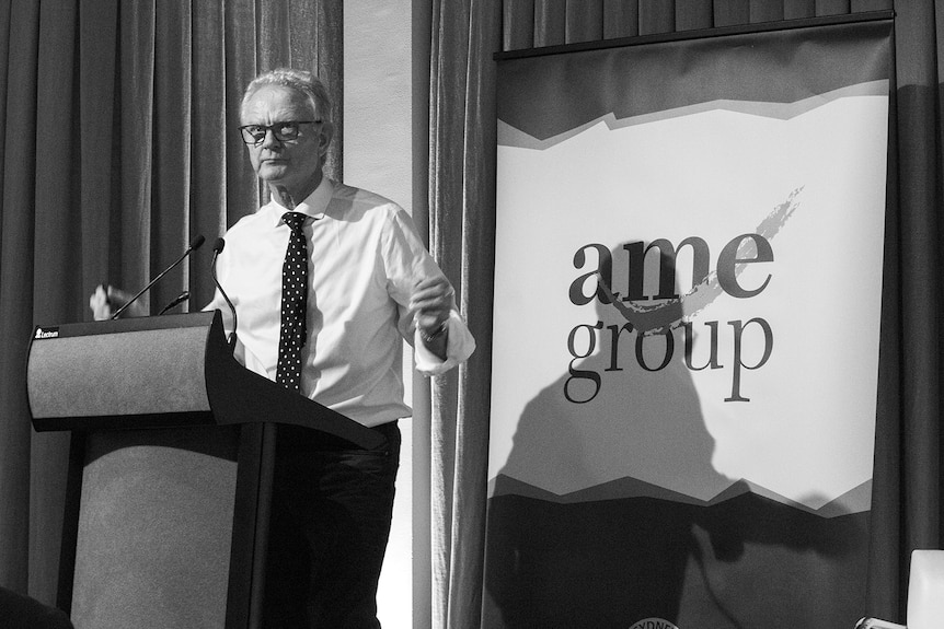 A black and white photo of Julian Malnic in front of an AME Group banner on a stage.