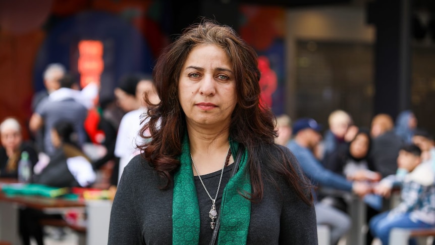 A mid-shot of a woman wearing a green scarf with people at a rally in the background.