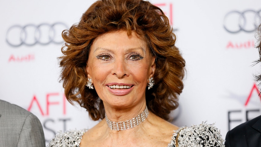 Sophia Loren smiles in formal wear on a red carpet