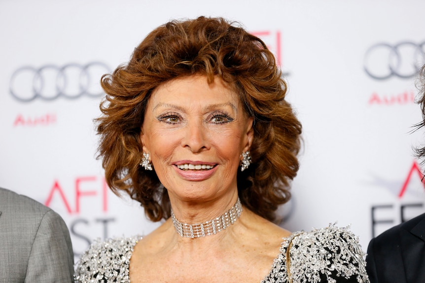 Sophia Loren smiles in formal wear on a red carpet