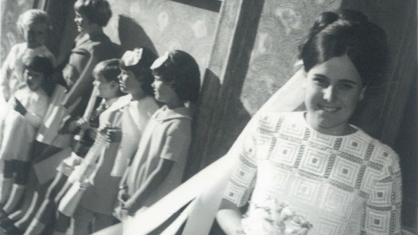 A 1960s bride in a geometrical print dress with a group of children in the background.