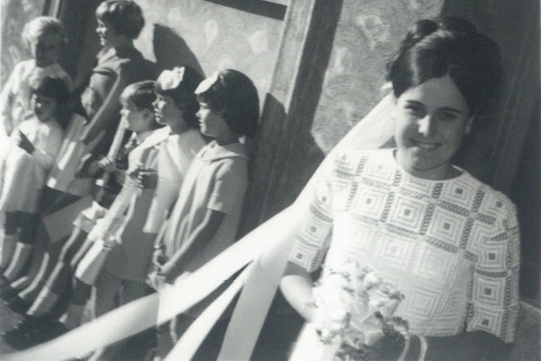 A 1960s bride in a geometrical print dress with a group of children in the background.