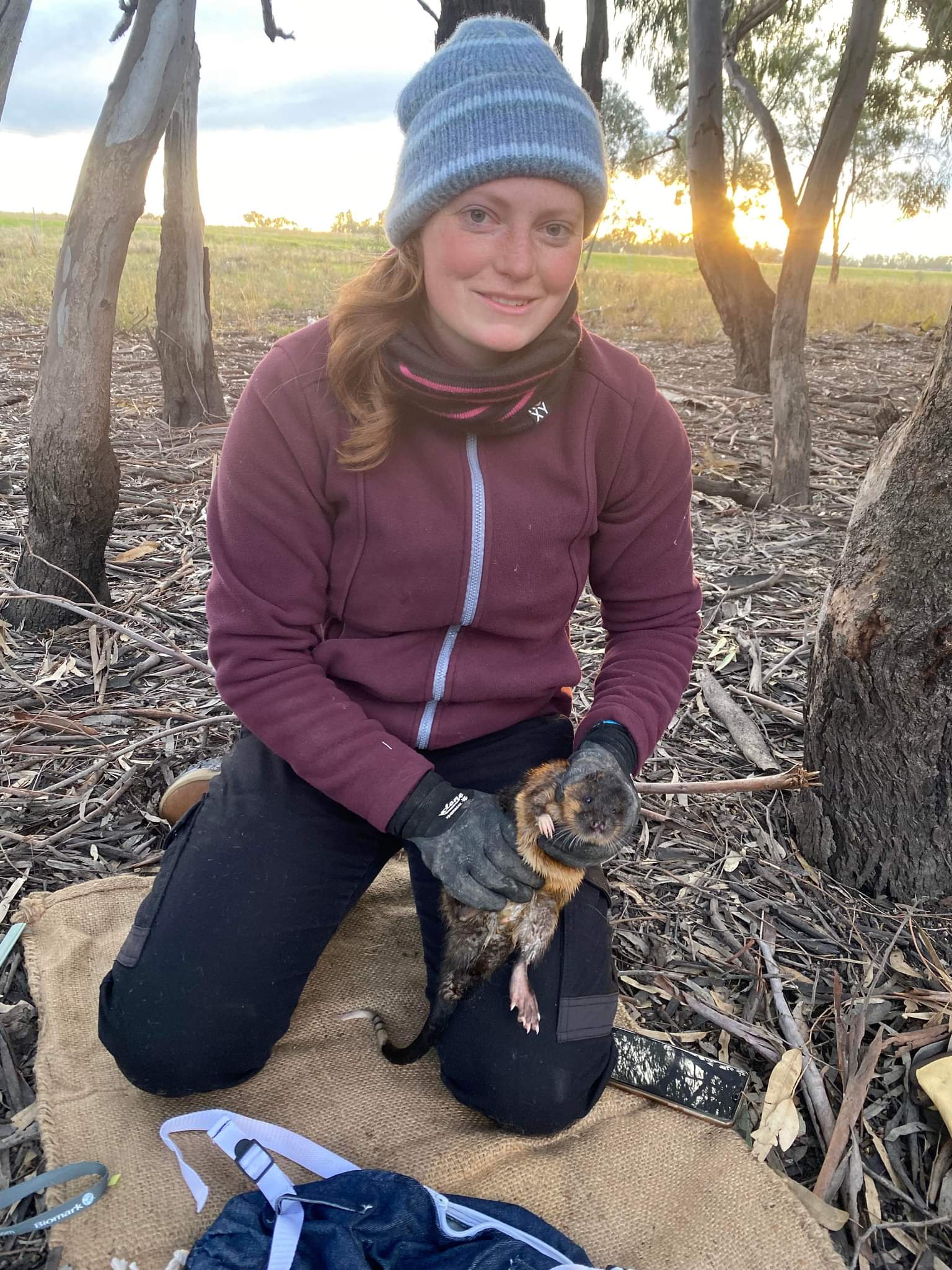 A woman squatting and holding a rat-like creature in the forest