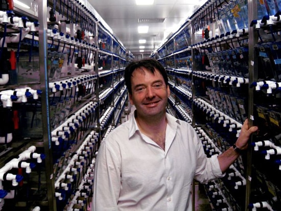 Um homem de camisa branca parado em um corredor cheio de aquários.