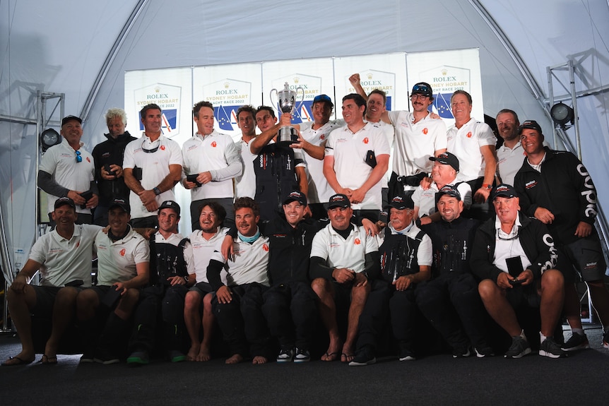 A team of men surround a silver cup trophy.