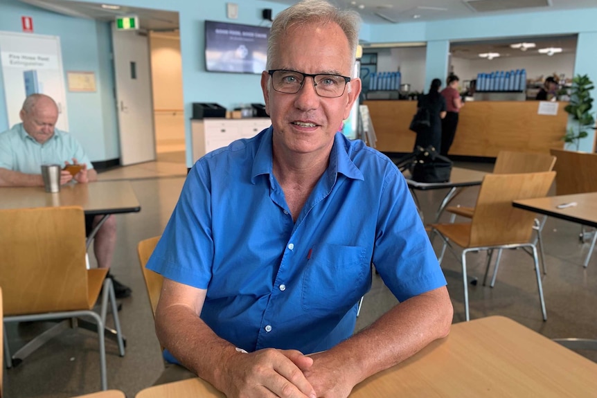 Ian Munro sits looking at the camera at a table in a hospital cafe.