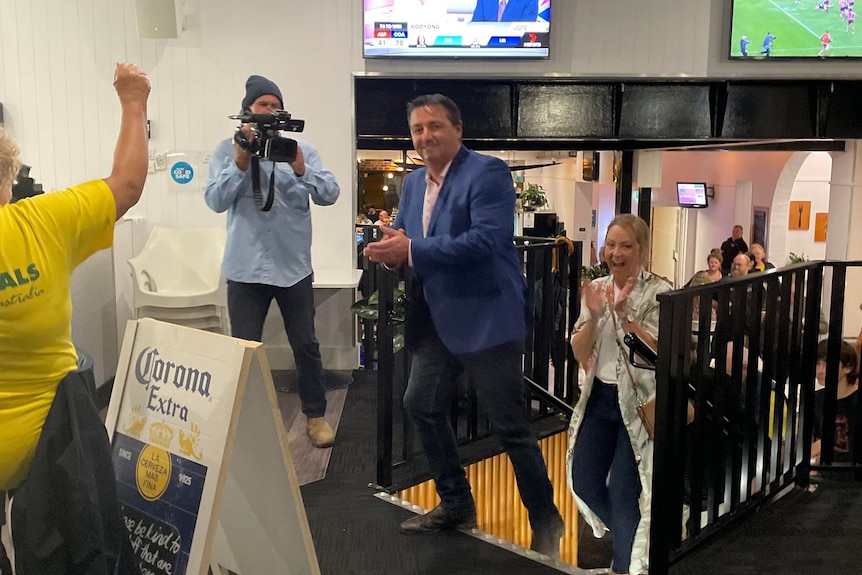 A man in a suit arrives at a function to applause and media cameras 