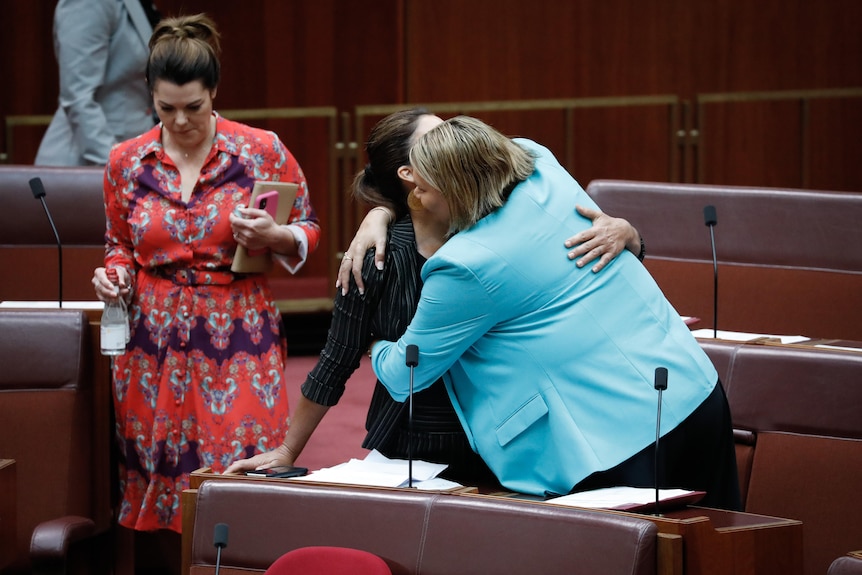 Dorinda Cox and Lidia Thorpe hug over their desks in Parliament chambers.