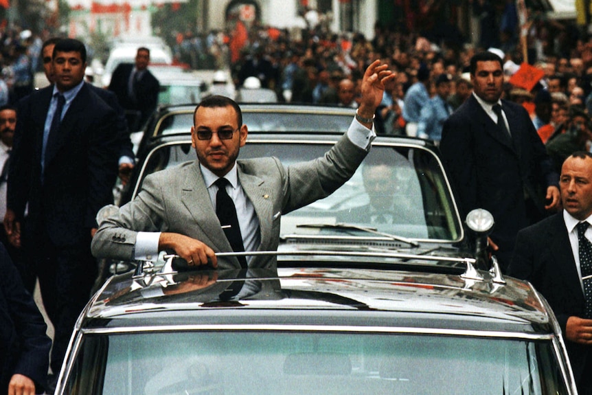 King Mohammed VI waves to the crowd frin a car during a street procession.