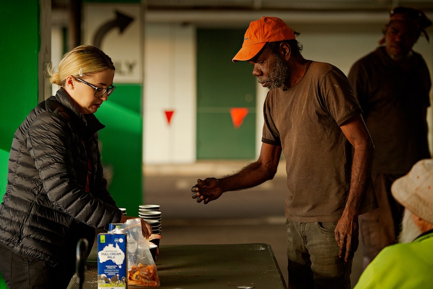 A charity worker is making a cup of coffee for a man at a community breakfast 